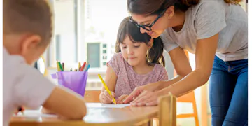 Teacher assisting a young girl with an activity in a secure and nurturing classroom, highlighting the importance of a safe learning environment in early childhood education.