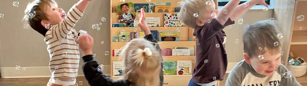 Children at Little Sunshine's Playhouse playing with bubbles in a classroom.