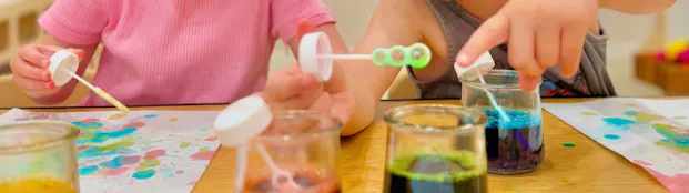Two children use bubble blowers to enhance their fine motor skills and create art!