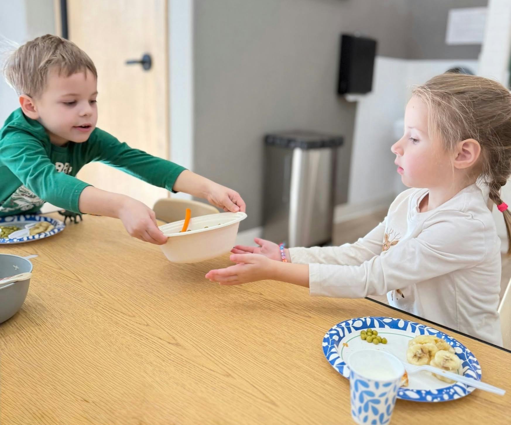 This photo, in which a little boy hands a bowl of food to his fellow classmate, is a good example of family style dining!