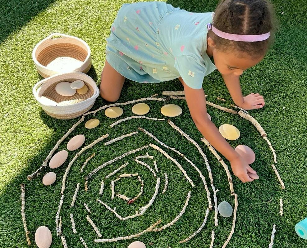 Depicted is a little girl placing stones in a loose parts mosaic on our Little Sunshine's Playhouse playground!